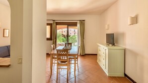 A dining area with a table and chairs, a cabinet with a television, and a view of a building through a window. - 60 sq m - Living room with kitchenette and double sofa bed, double bedroom, bathroom with bidet and showeror bathtub.<br>Ground floor with furnished veranda.<br>Equipped with:<br>- tv <br>- washing machine<br>- 1 beach umbrella<br>- iron and ironing boar (Stintino)
