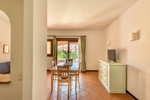 Un coin repas avec une table et des chaises, un meuble contenant un téléviseur, et une vue sur un bâtiment par la fenêtre.
