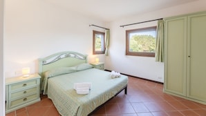 A bedroom with a bed, nightstands, a wardrobe, and a window with curtains. - 60 sq m - Living room with kitchenette and double sofa bed, double bedroom, bathroom with bidet and showeror bathtub.<br>Ground floor with furnished veranda.<br>Equipped with:<br>- tv <br>- washing machine<br>- 1 beach umbrella<br>- iron and ironing boar (Stintino)