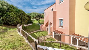 A building with a pink facade, a wooden fence, and a well-maintained lawn. - 60 sq m - Living room with kitchenette and double sofa bed, double bedroom, bathroom with bidet and shower or bath, access to communal pool. <br>Ground floor or first floor with furnished veranda or balcony.<br>Equipped with:<br>- tv <br>- washing machin (Stintino)
