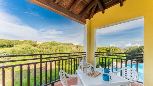 A balcony with a table and chairs, overlooking a swimming pool and greenery. - 60 sq m - Living room with kitchenette and double sofa bed, double bedroom, bathroom with bidet and shower or bath, access to communal pool. <br>Ground floor or first floor with furnished veranda or balcony.<br>Equipped with:<br>- tv <br>- washing machin (Stintino)