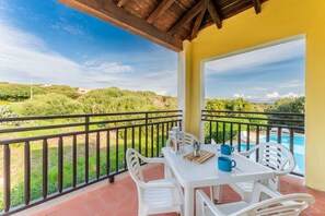 A balcony with a table and chairs, overlooking a swimming pool and greenery. - 60 sq m - Living room with kitchenette and double sofa bed, double bedroom, bathroom with bidet and shower or bath, access to communal pool. <br>Ground floor or first floor with furnished veranda or balcony.<br>Equipped with:<br>- tv <br>- washing machin (Stintino)