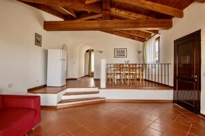 A spacious living area with a red sofa, a white refrigerator, a dining table with chairs, and a staircase leading to a balcony.