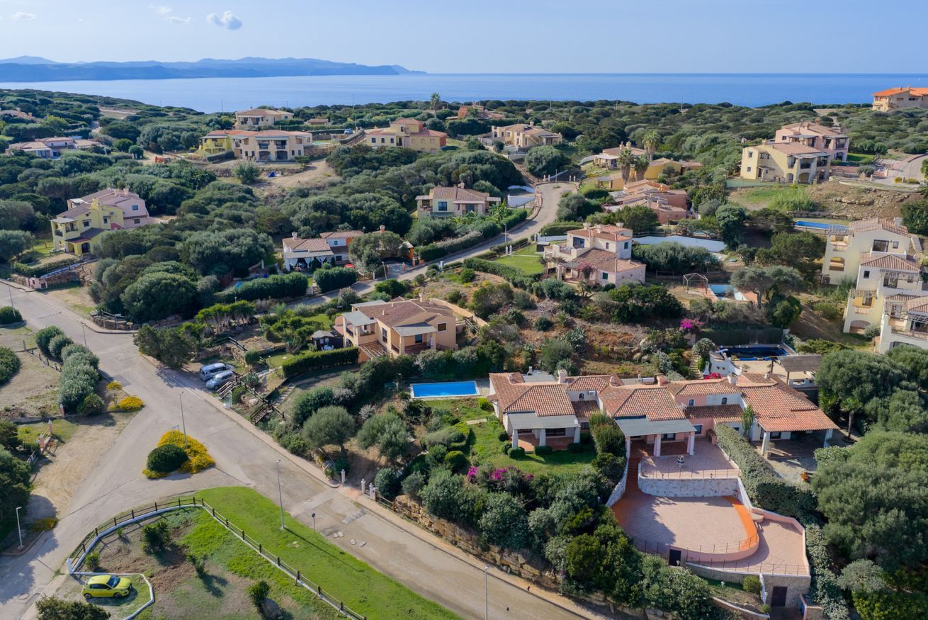 An aerial view of a coastal residential area with houses, a swimming pool, and a curved driveway.