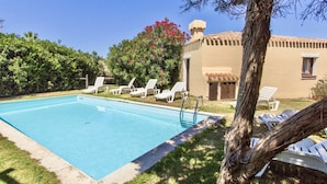 A swimming pool with lounge chairs and a building with a tiled roof.