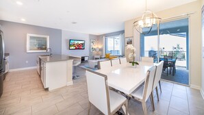 Una cocina moderna con una isla central, un comedor con una mesa grande y sillas, y una sala de estar con un sofá y una mesa de centro.