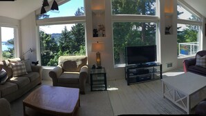 Un salon spacieux doté d’un grand téléviseur, de sièges confortables et offrant une vue sur l’extérieur.