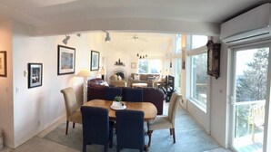 Un salon spacieux doté d’une cheminée, un coin repas avec une table et des chaises, et de grandes fenêtres laissant entrer la lumière naturelle.