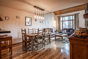 A cozy living room with wooden furniture, a dining area, and a large window with curtains.