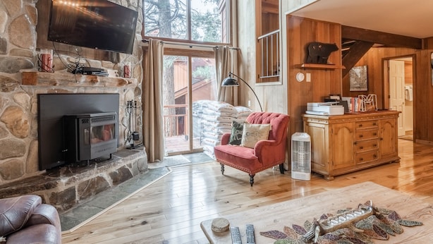 Ein gemütliches Wohnzimmer mit Kamin aus Stein, einem Flachbildfernseher, einem roten Sessel und einem Holzkabinett.