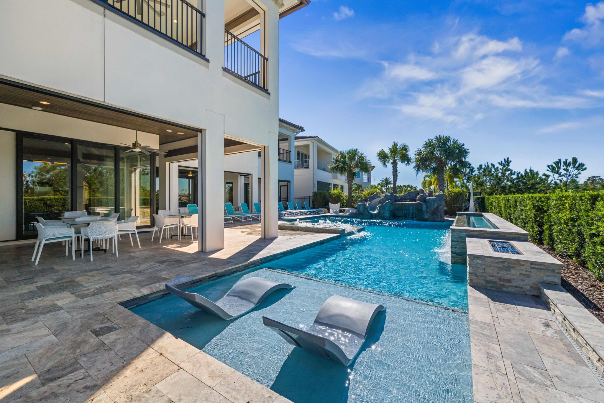 A modern outdoor pool area with lounge chairs, a dining set, and a waterfall feature.