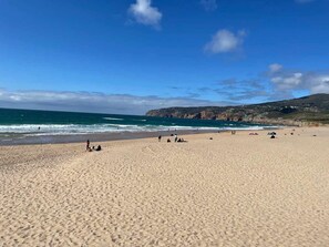 A wide sandy beach with a clear blue sky and calm sea.