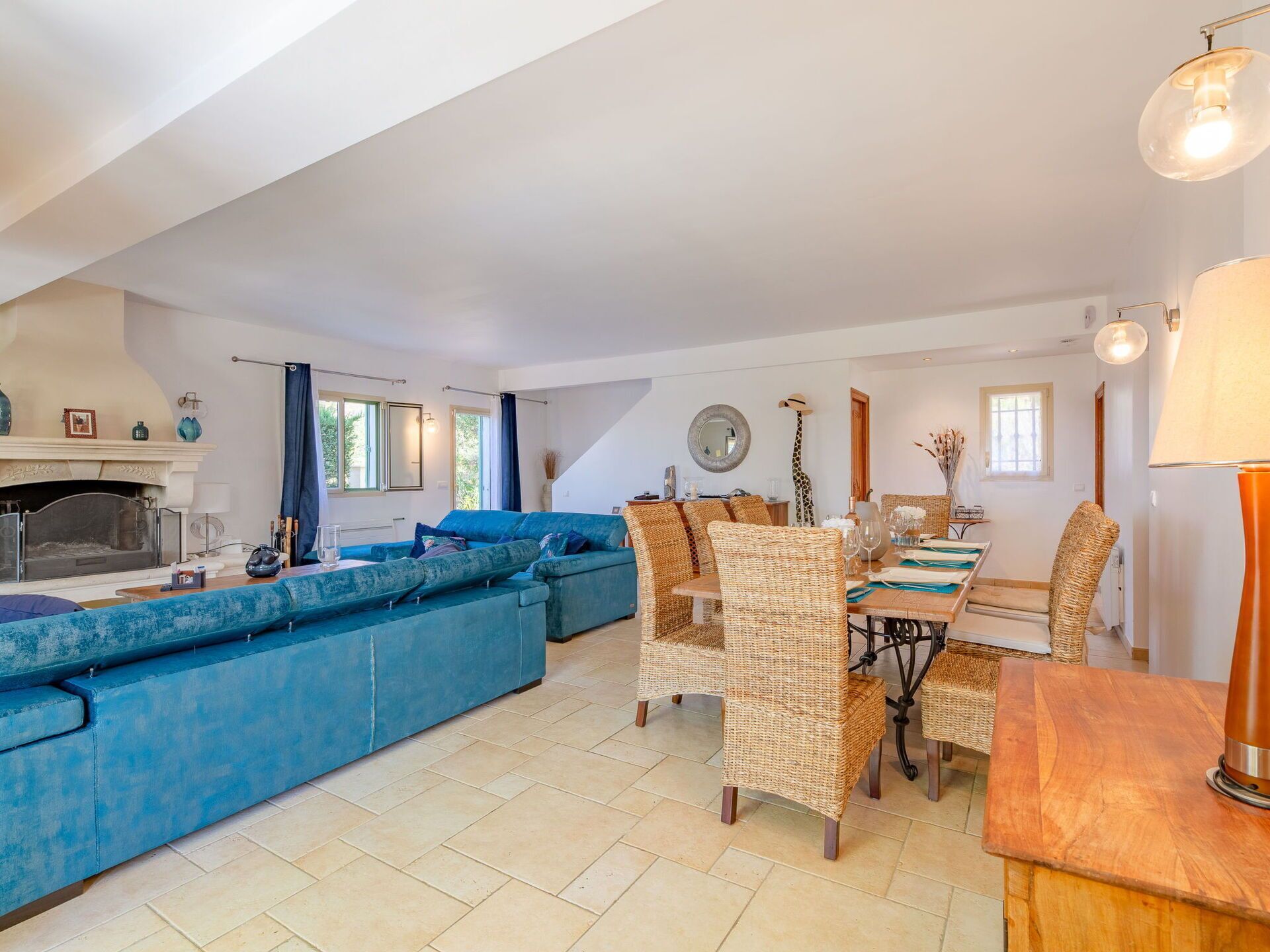 Un salón espacioso con un sofá azul, sillones de mimbre, una mesa de comedor y una chimenea.