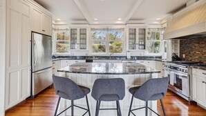A modern kitchen with white cabinetry, a large island, and three bar stools.