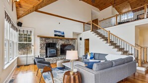 A spacious living room with a stone fireplace, a grey sofa, and a wooden staircase.