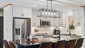 Una cocina moderna con armarios blancos, electrodomésticos de acero inoxidable y una isla central con asientos tipo barra.