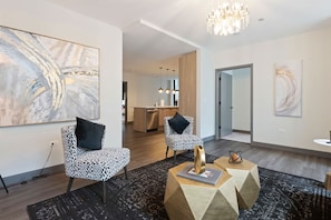 Un salón moderno con sillones de estampado de leopardo, arte abstracto, una araña y una cocina al fondo.