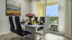 Un comedor con una mesa dispuesta para cuatro personas, con sillas negras, un florero con flores rosadas y copas de vino y jugo.