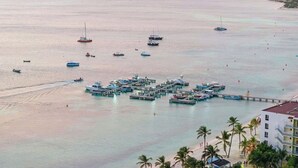 Una marina con varias embarcaciones amarradas, un muelle que se adentra en el agua y un hotel frente a la playa en primer plano.