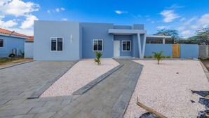 Una casa moderna a due piani con facciata blu, vialetto in ghiaia e un piccolo giardino con palme.