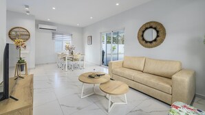 Un soggiorno moderno con un divano color beige, due tavolini rotondi, un'area pranzo con tavolo e sedie, e un grande specchio a parete.