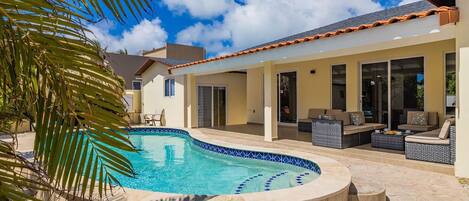 A pool area with a curved edge, outdoor seating, and a covered patio.