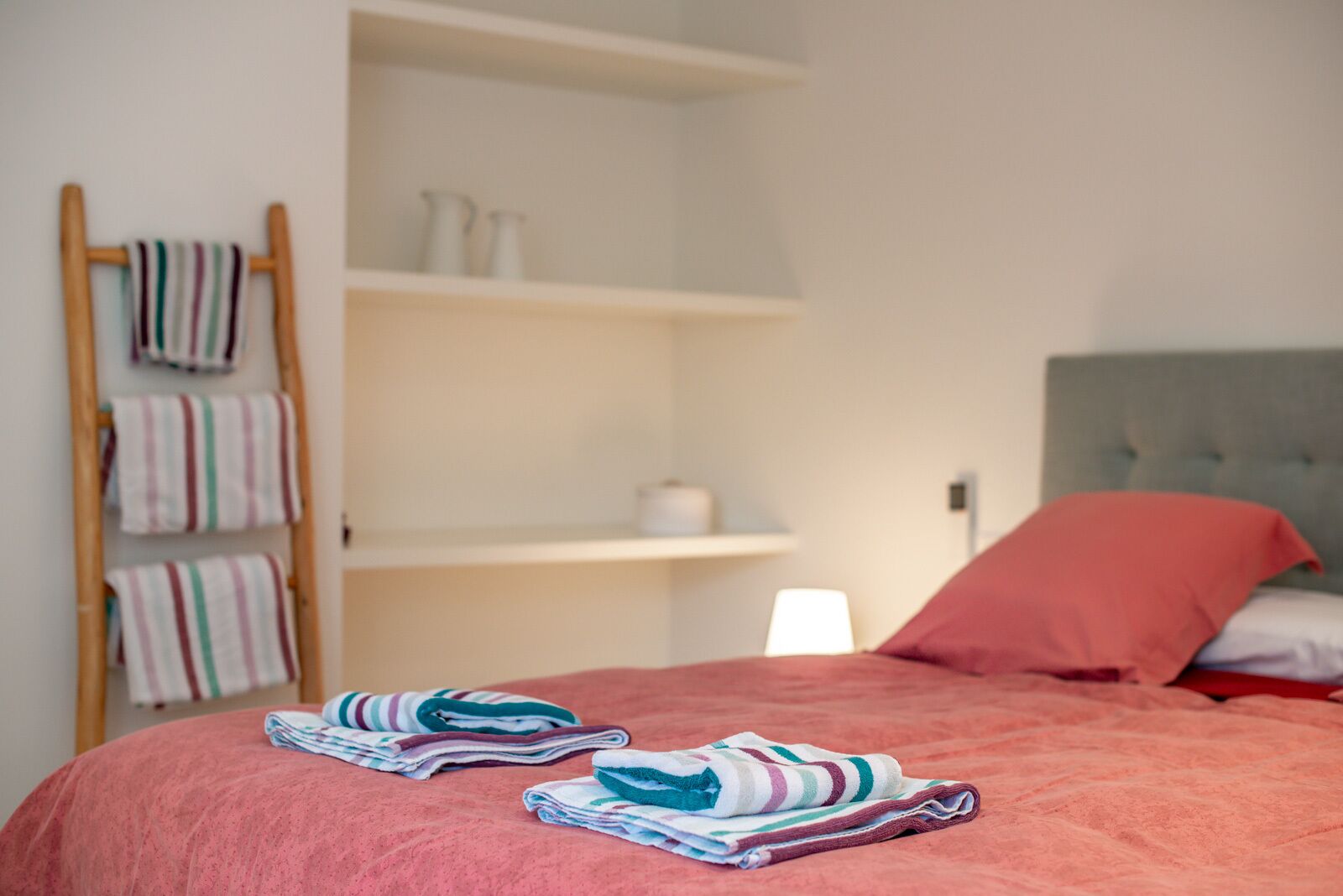 A neatly made bed with striped towels, a grey headboard, and a red pillow.