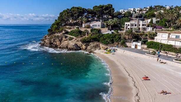 Un pueblo costero con una playa de arena, mar azul cristalino y edificios en una ladera.