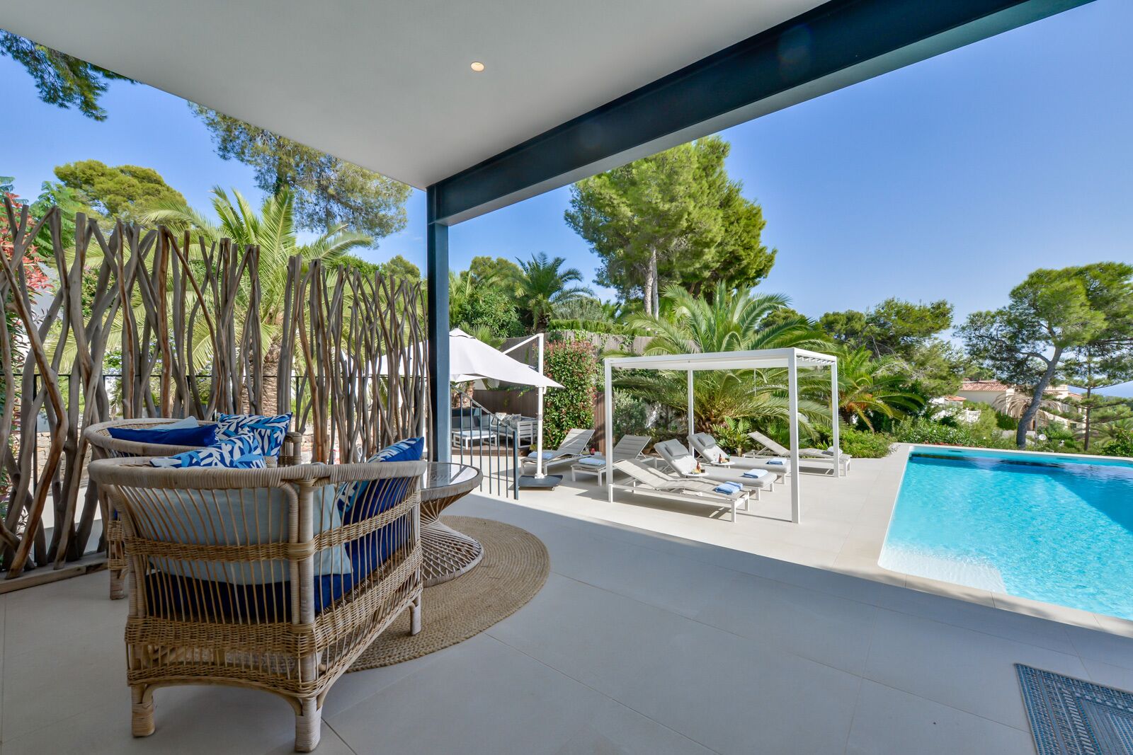 A modern outdoor area with a pool, wicker furniture, and a pergola.