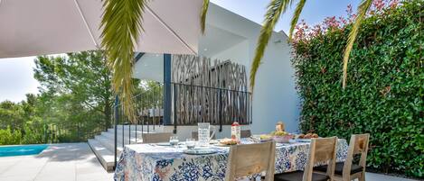 An outdoor dining area with a table set for four, surrounded by chairs, under a large umbrella.