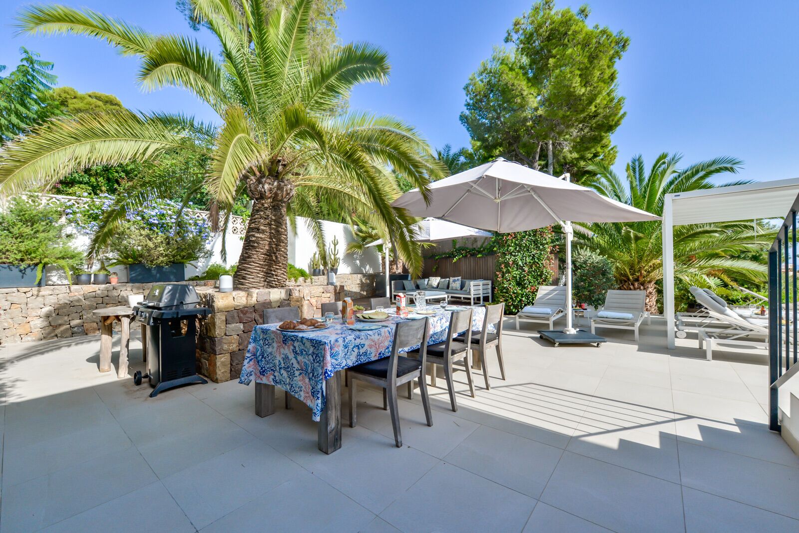 An outdoor patio with a grill, dining table, and lounge chairs.