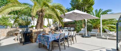 An outdoor patio with a grill, dining table, and lounge chairs.