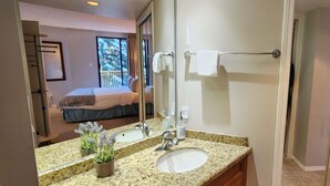 Un baño de hotel con encimera de granito, un lavamanos, un espejo y un perchero para toallas.