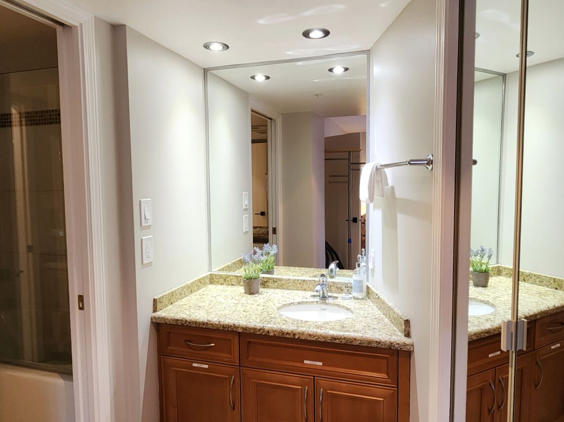 A bathroom with a granite countertop, a sink, a mirror, and wooden cabinets.