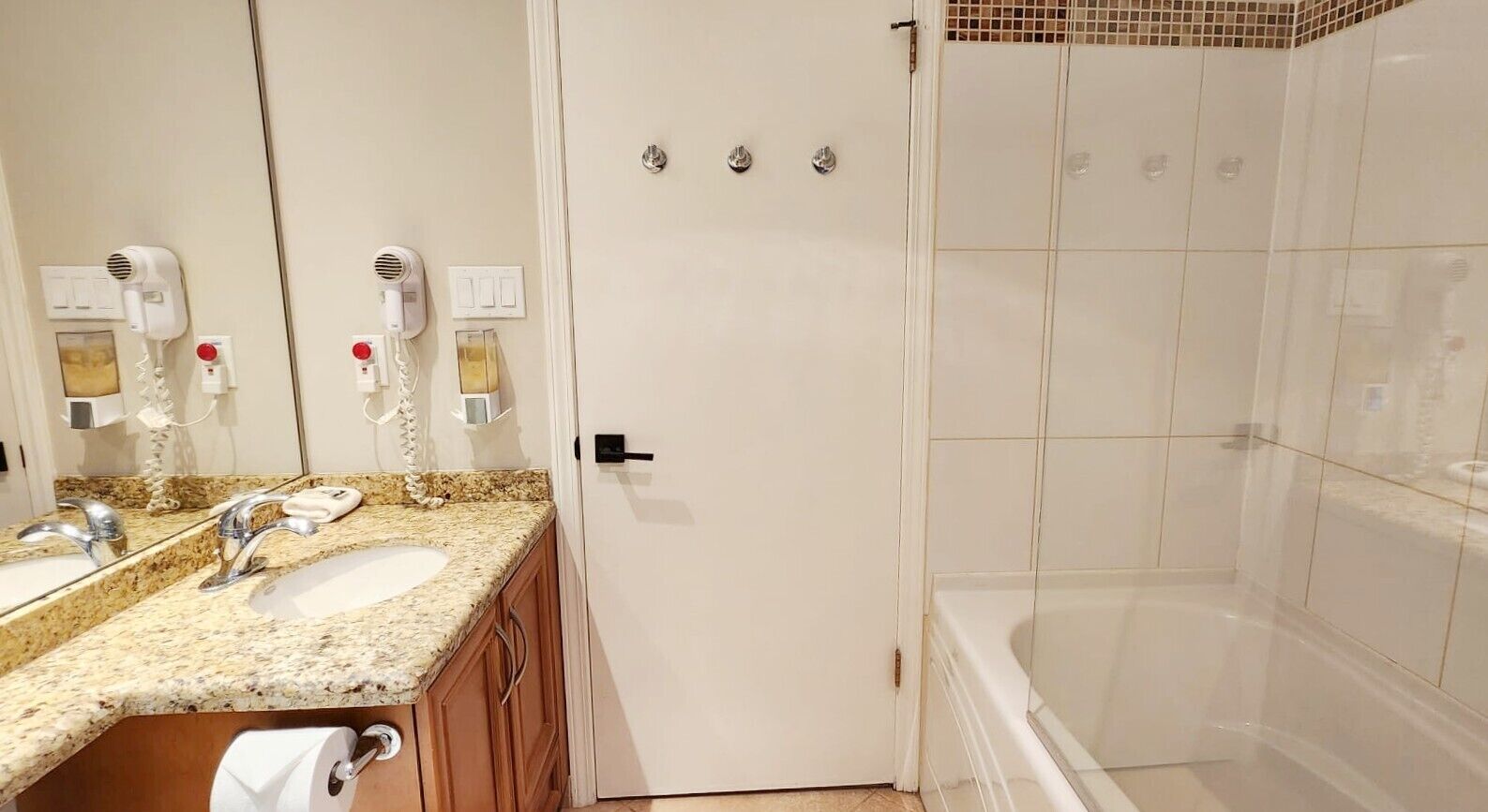 A bathroom with a double sink, a mirror, a hairdryer, a towel rack, and a shower area.