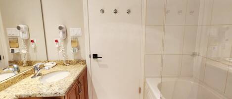 A bathroom with a double sink, a mirror, a hairdryer, a towel rack, and a shower area.