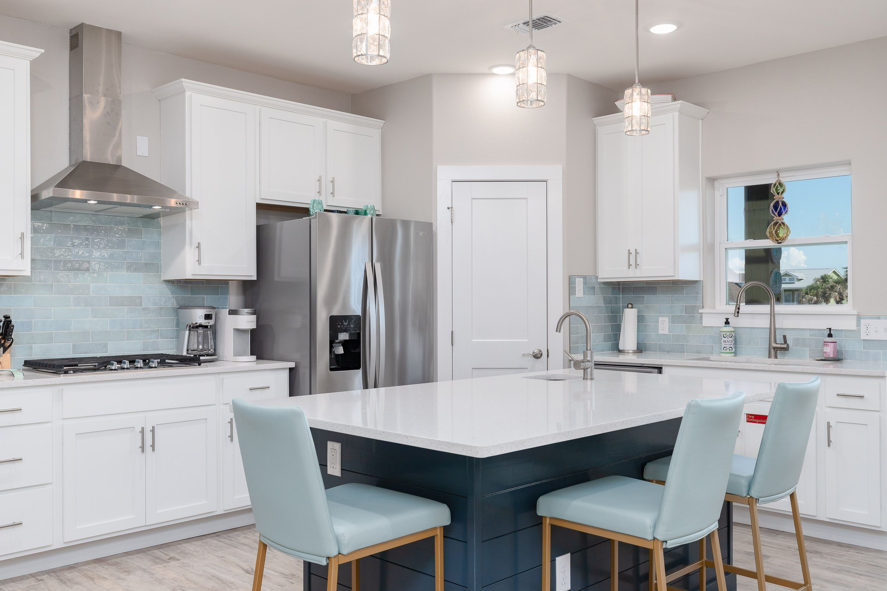 A modern kitchen with white cabinets, stainless steel appliances, a large island with bar stools, and pendant lighting.