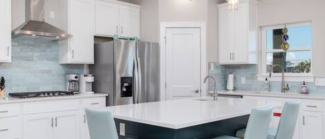 A modern kitchen with white cabinets, stainless steel appliances, a large island with bar stools, and pendant lighting.