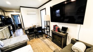 Un salon moderne comprenant un canapé, un téléviseur fixé au mur, une cheminée et un coin repas avec une table et des chaises.