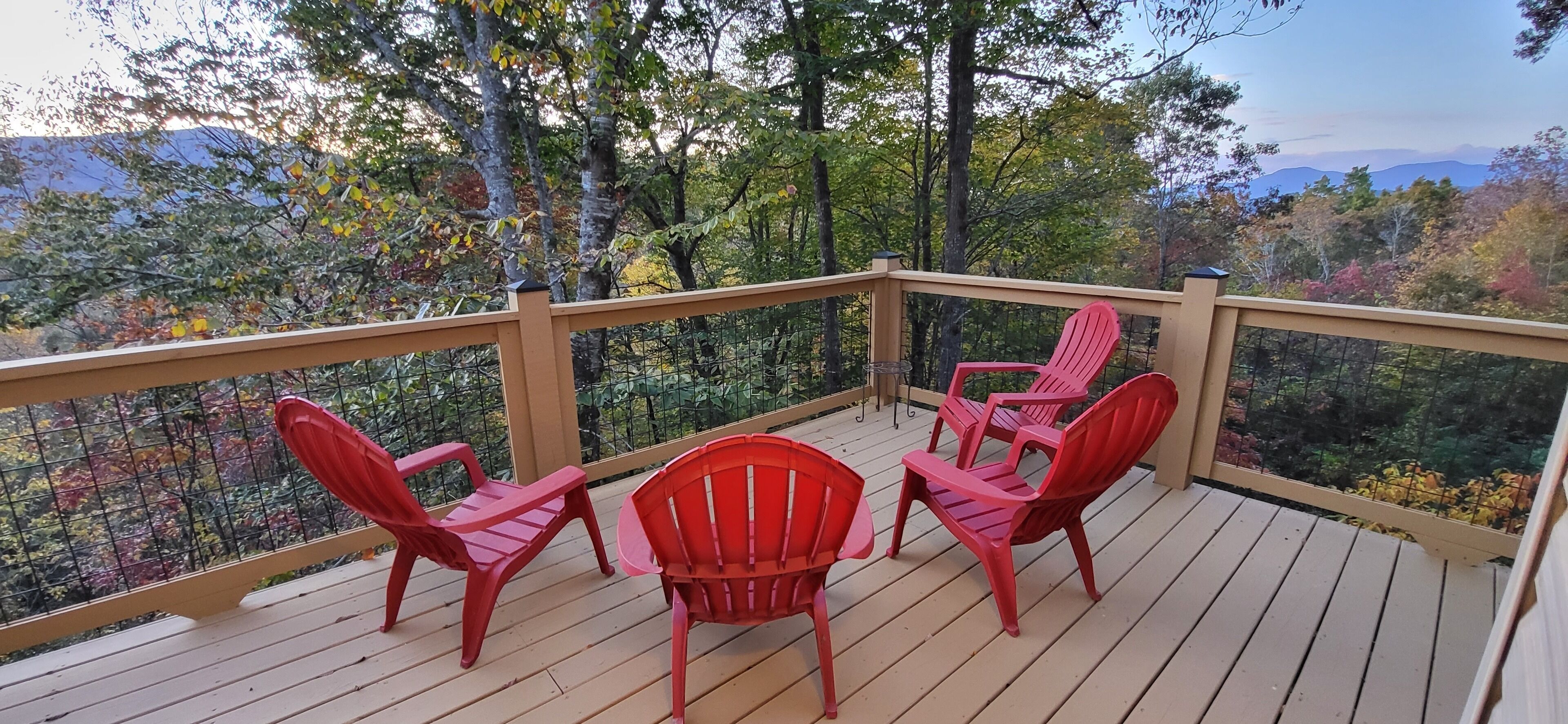 Eine Holzterrasse mit Geländer, ausgestattet mit vier roten Adirondack-Stühlen und einem kleinen Tisch.