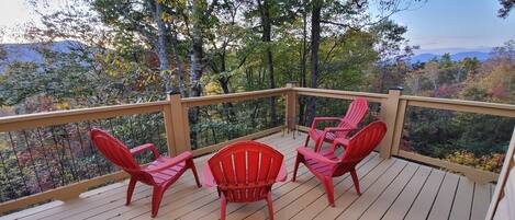 Eine Holzterrasse mit Geländer, ausgestattet mit vier roten Adirondack-Stühlen und einem kleinen Tisch.