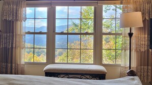 A bedroom with a large window, a bedside table, a lamp, and a dresser. - Cozy Mountain Chalet with views, private setting! Near WCU and Castle Ladyhawke  (Cullowhee)