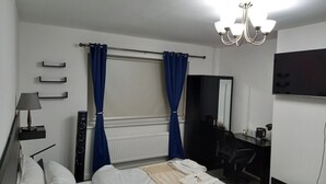 A hotel room with a bed, a desk, a chair, a lamp, a mirror, and a TV.