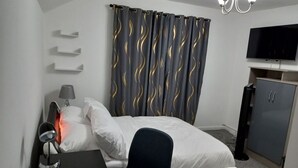 A hotel room with a bed, a desk with a lamp, a chair, a TV, and a wardrobe.