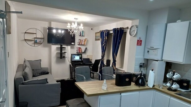 A compact living space with a sofa, a small kitchen area, a dining table, and a TV mounted on the wall.