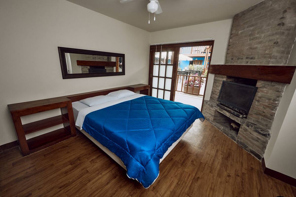 Ein Schlafzimmer mit Bett, Holz-Kopfteil, Kamin und Blick auf den Balkon.