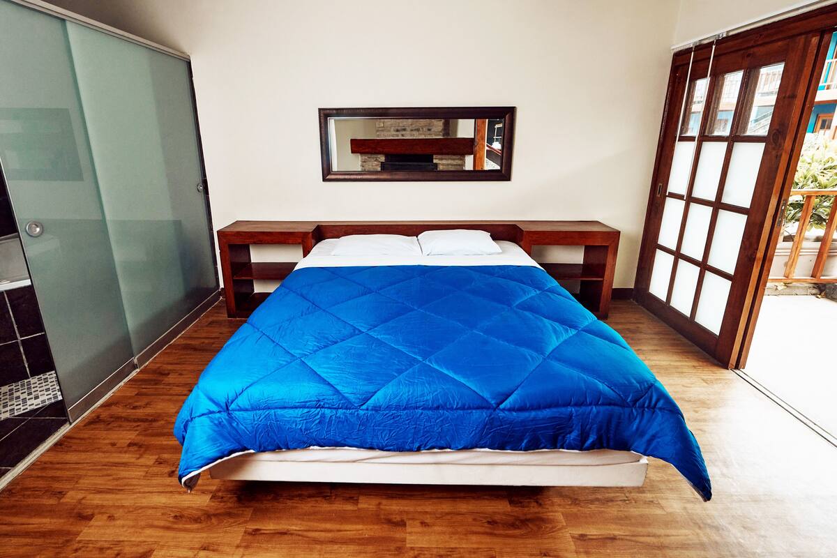 Ein Schlafzimmer mit einem Bett, einer hölzernen Bank, einem Glastischschrank und einem großen Spiegel an der Wand.