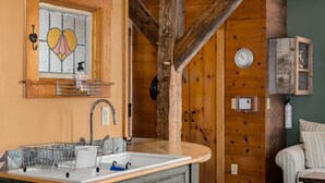 Een rustiek houten interieur met een gootsteen, een afdruiprek, een klok aan de muur en een klein kastje.