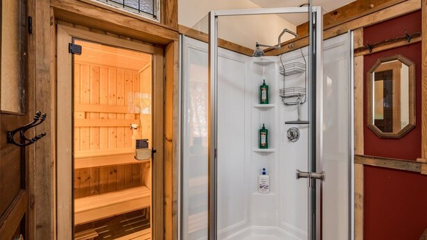 Een houten sauna met een glazen deur, een douchegedeelte met planken en een rode muur met een spiegel.