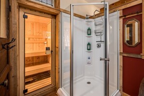 Eine Holzsauna mit Glastür, einer Duschkabine mit Ablagen und einer roten Wand mit Spiegel.